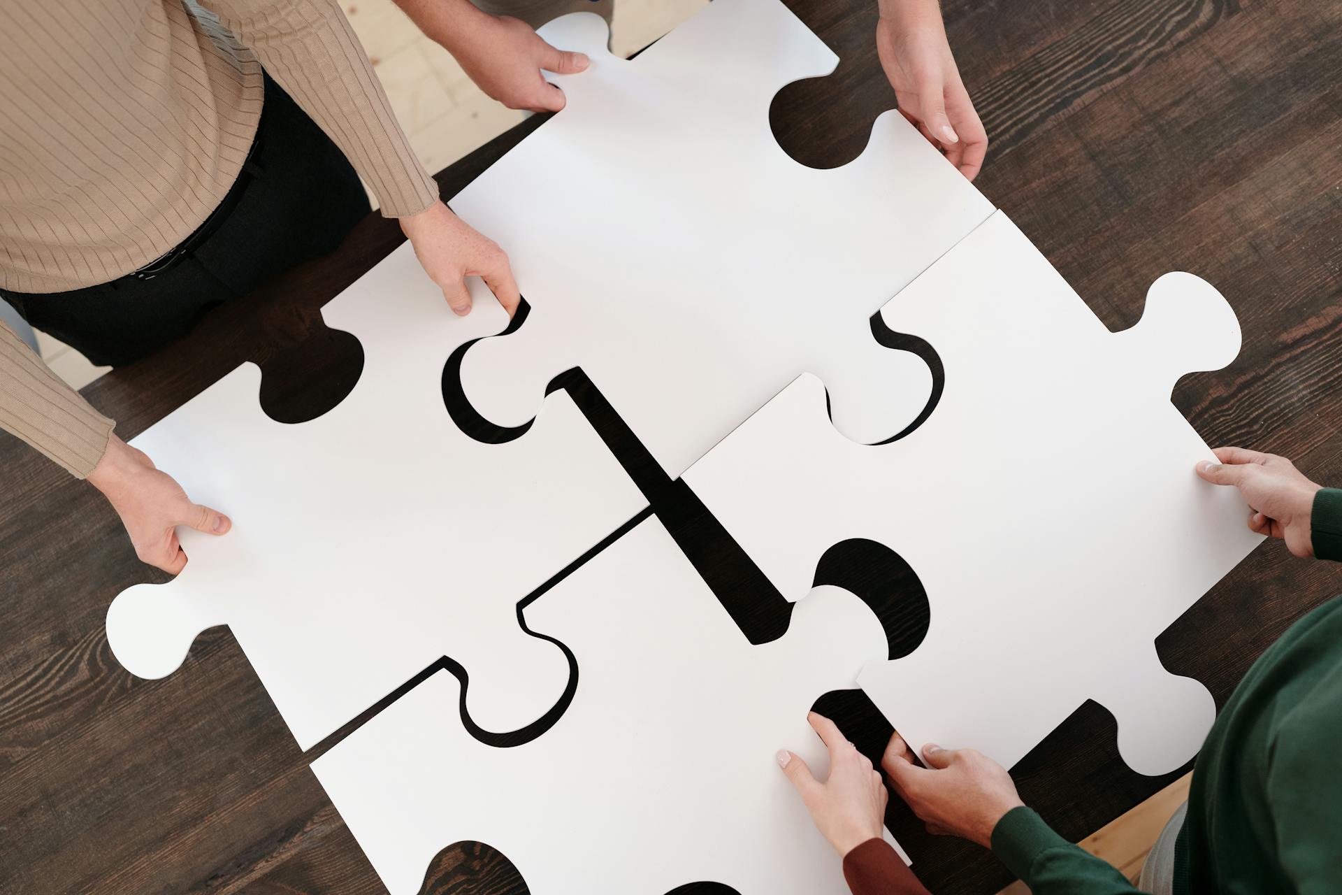 A group of four people, each holding a piece of a jigsaw puzzle, working together to complete the image.