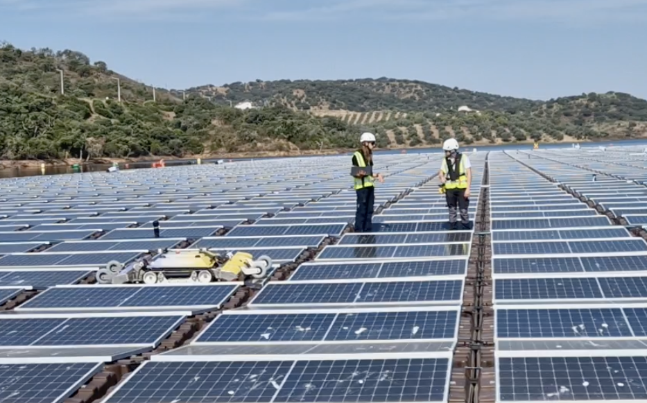 Two people working alongside a cleaning robot on a floating photovoltaic platform